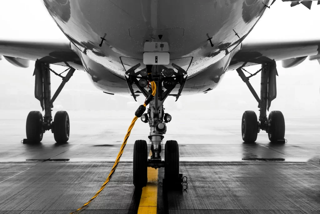 Close-up view of an airplane's landing gear and nose section on the tarmac, featuring a yellow tow cable connected to the aircraft.